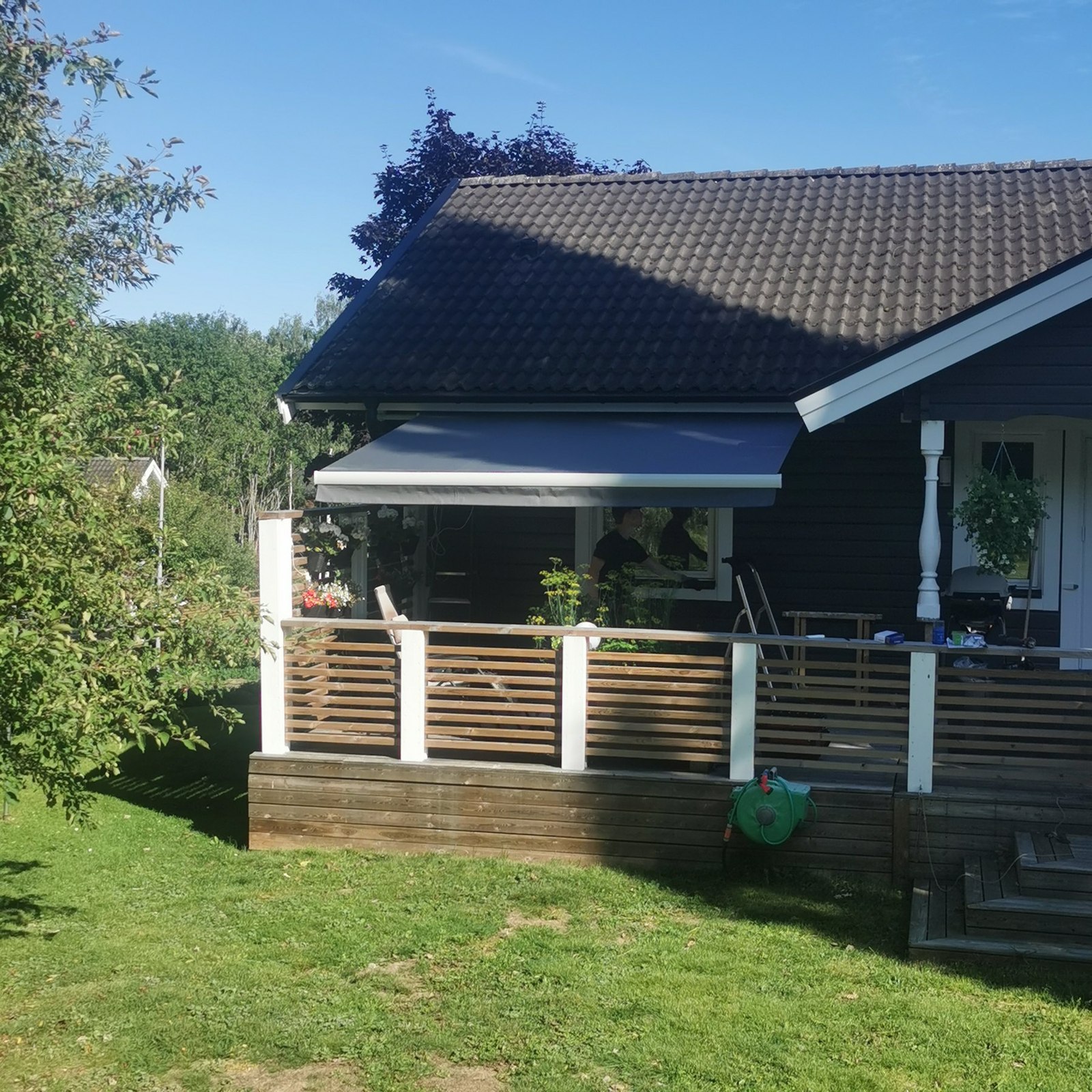 Mörk terrassmarkis utfälld över en altan med träräcke vid ett hus