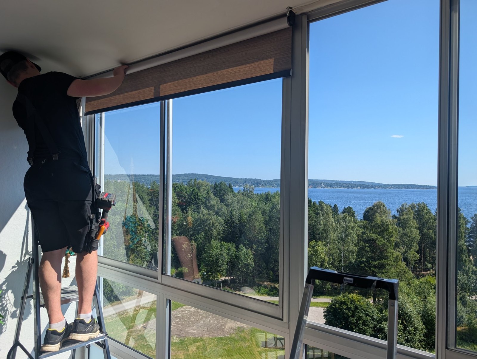 Montör på stege som monterar en rullgardin på en inglasad balkong