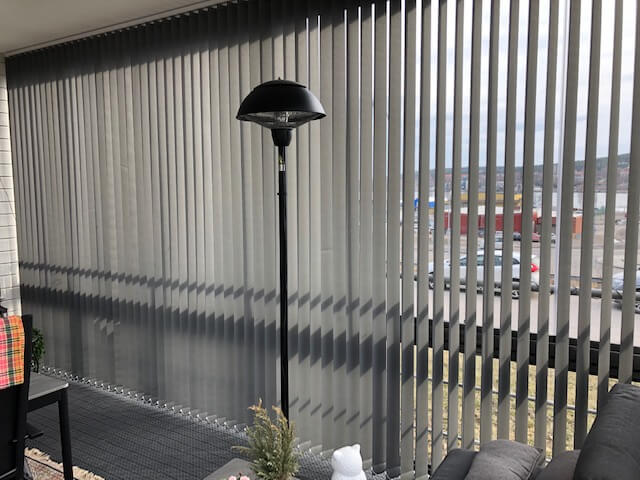 Ljusa lamellgardiner längs glaspartiet på en inglasad balkong med en terrassvärmare