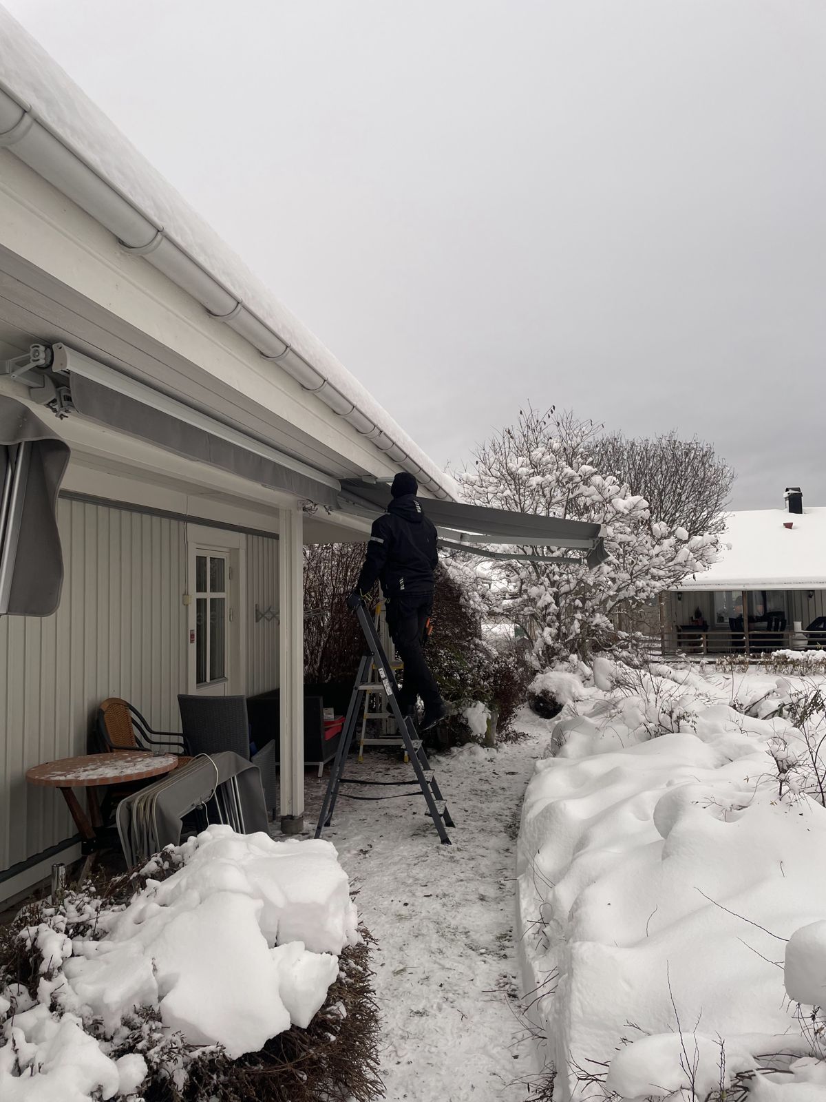 Montör på stege som monterar en markis på ett snötäckt hus