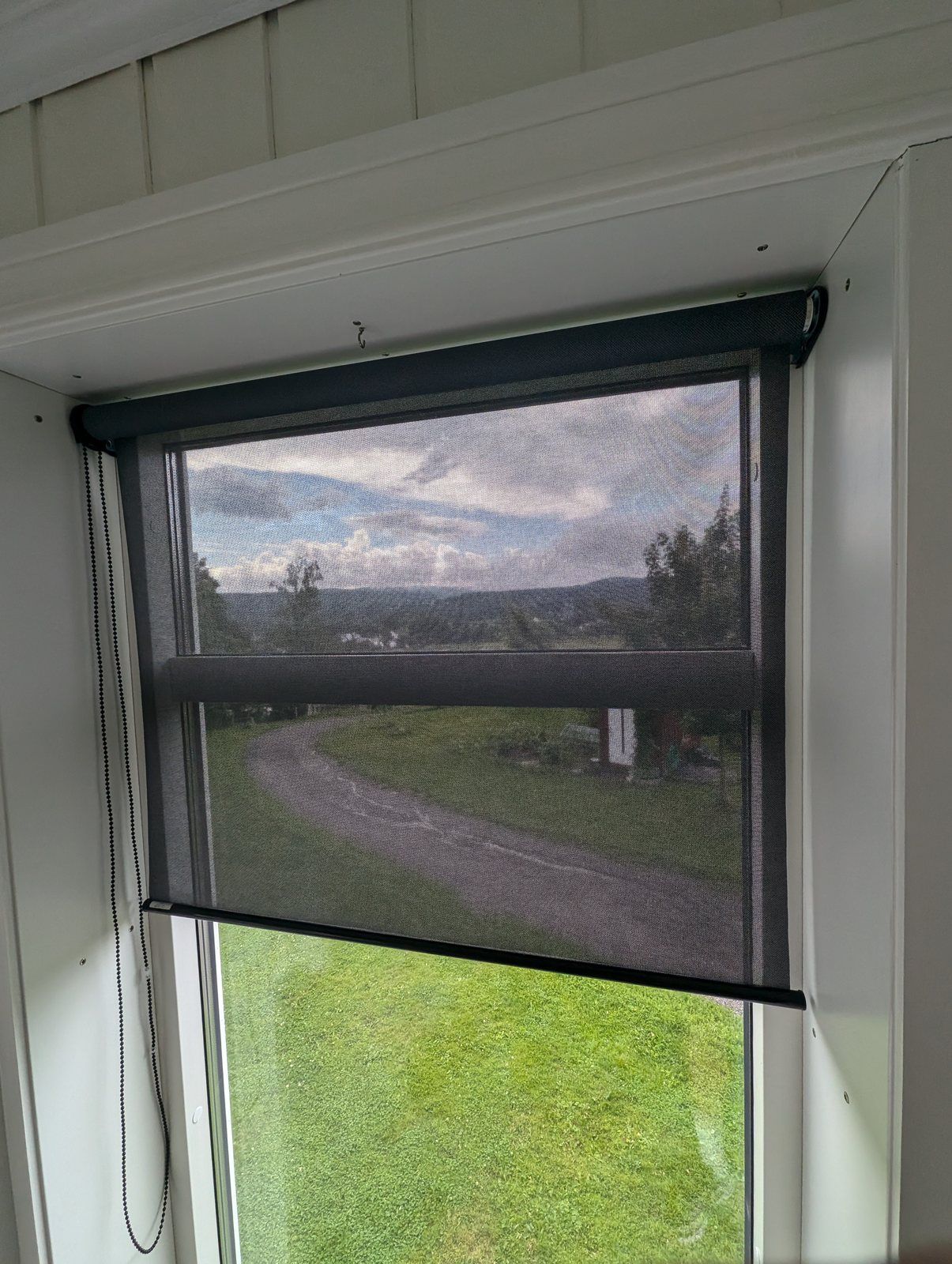 Mörk screenrullgardin halvvägs neddragen framför ett fönster